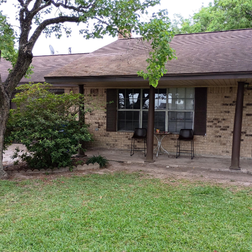 Side view of Sue Drive home with covered porch, mature oak trees, and lawn seating area